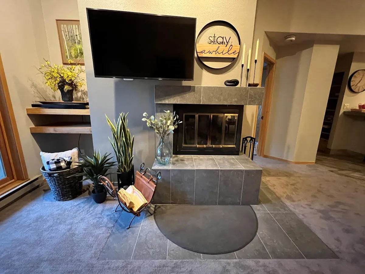 An inviting living space with a glowing fireplace, a large television, comfortable seating, decorative touches, and lush plants that create a welcoming atmosphere for gathering or unwinding after a day outside.