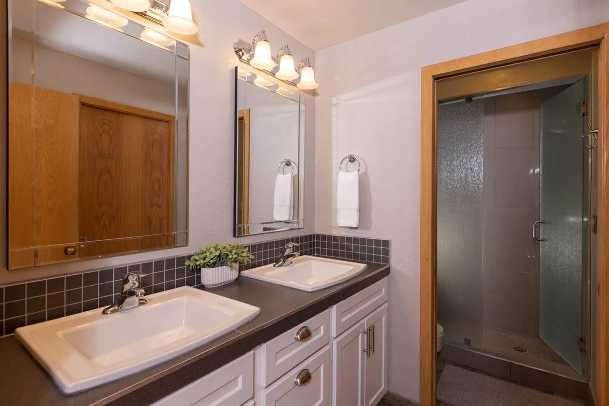 A modern bathroom featuring a double sink vanity, large mirrors, a glass-enclosed shower, and an organized towel rack. The space feels bright, clean, and functional, ideal for personal routines and privacy.