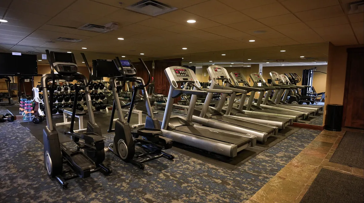 A modern, well-equipped fitness center featuring multiple treadmills, elliptical machines, a mirrored wall, and free weights, all set in a bright, motivational space ideal for maintaining your routine while on vacation.