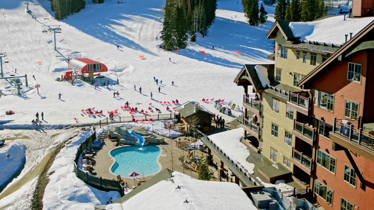 An energetic snapshot showing skiers gliding down the slopes, a group relaxing by the heated outdoor pool, and the resort buildings in the background, with the ski lift completing the picture of a full-featured mountain resort.
