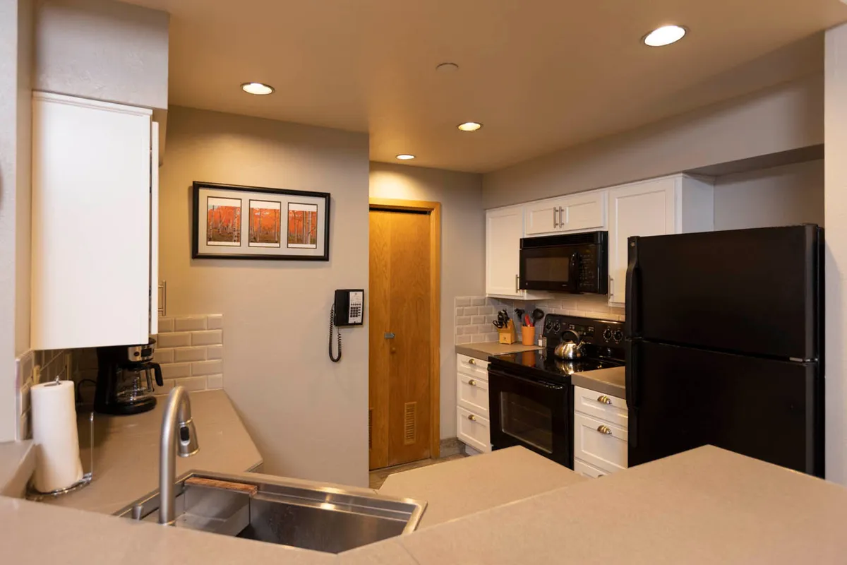 A view of the kitchen area showcasing a kitchen sink, black refrigerator, microwave, oven, and framed artwork. The scene feels cozy and functional, offering a clear look at the main appliances and workspaces.