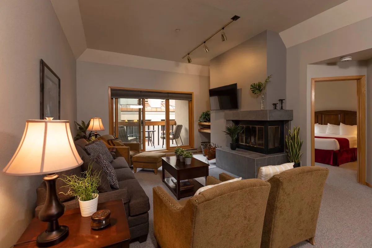 The photo captures a cozy living room corner with a fireplace, a large window showcasing the mountain scenery, comfortable seating, and a coffee table—ideal for relaxing, reading, or enjoying conversations. Soft lighting creates a warm, inviting mood.