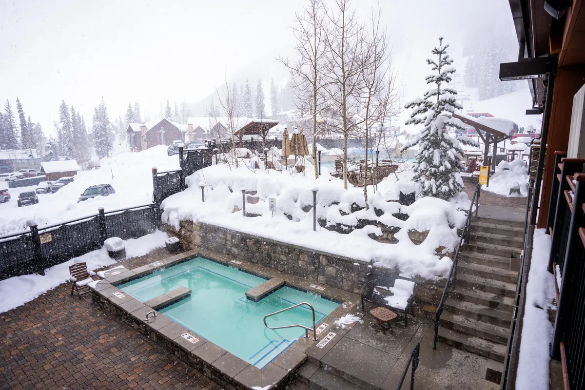 This exterior image features an outdoor hot tub nestled in a snow-covered landscape surrounded by trees. The hot tub is steaming, and guests are relaxing while enjoying a tranquil winter setting. The background hints at the serenity and rejuvenation offered by the rooftop hot tub amenity, especially after a day of skiing or exploring.