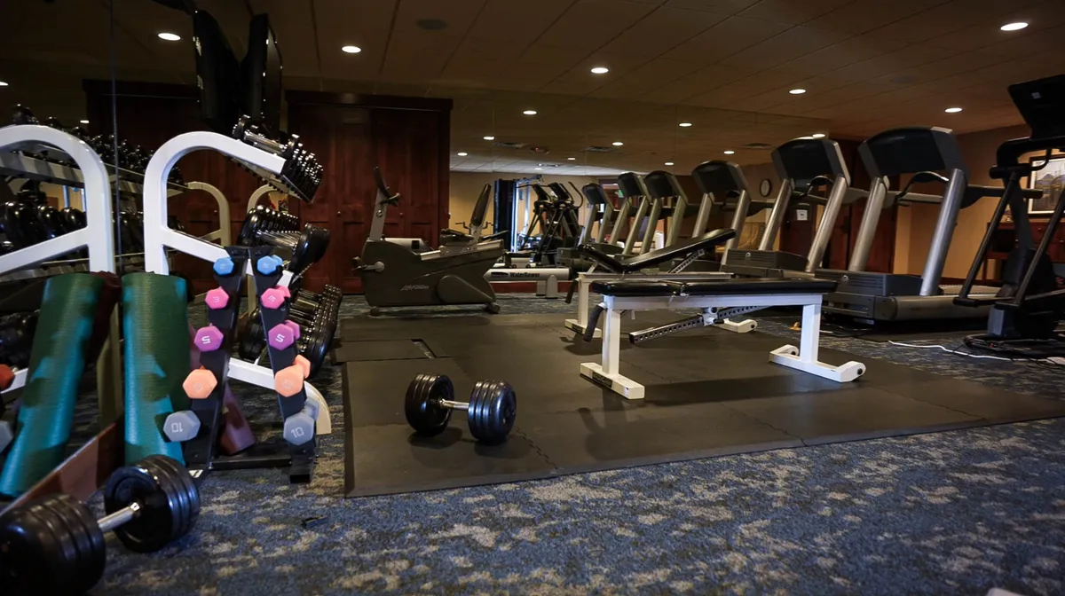 This interior image showcases a well-equipped fitness center featuring dumbbells, treadmills, and a weight bench. The space is bright and organized, encouraging guests to keep active during their stay. The overall feel is motivational and modern.